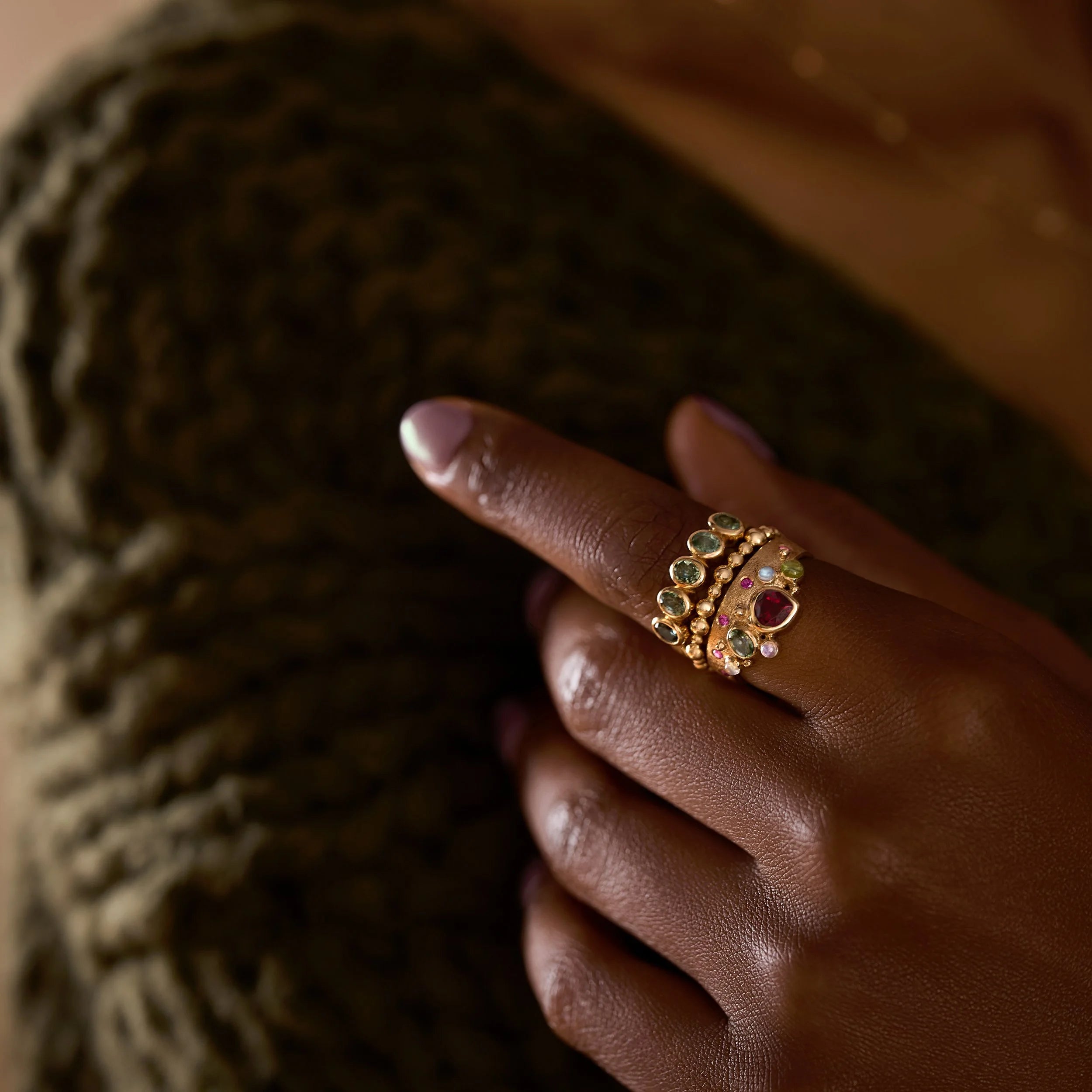 Close-up of a hand wearing a gold ring with gemstones against a textured background
