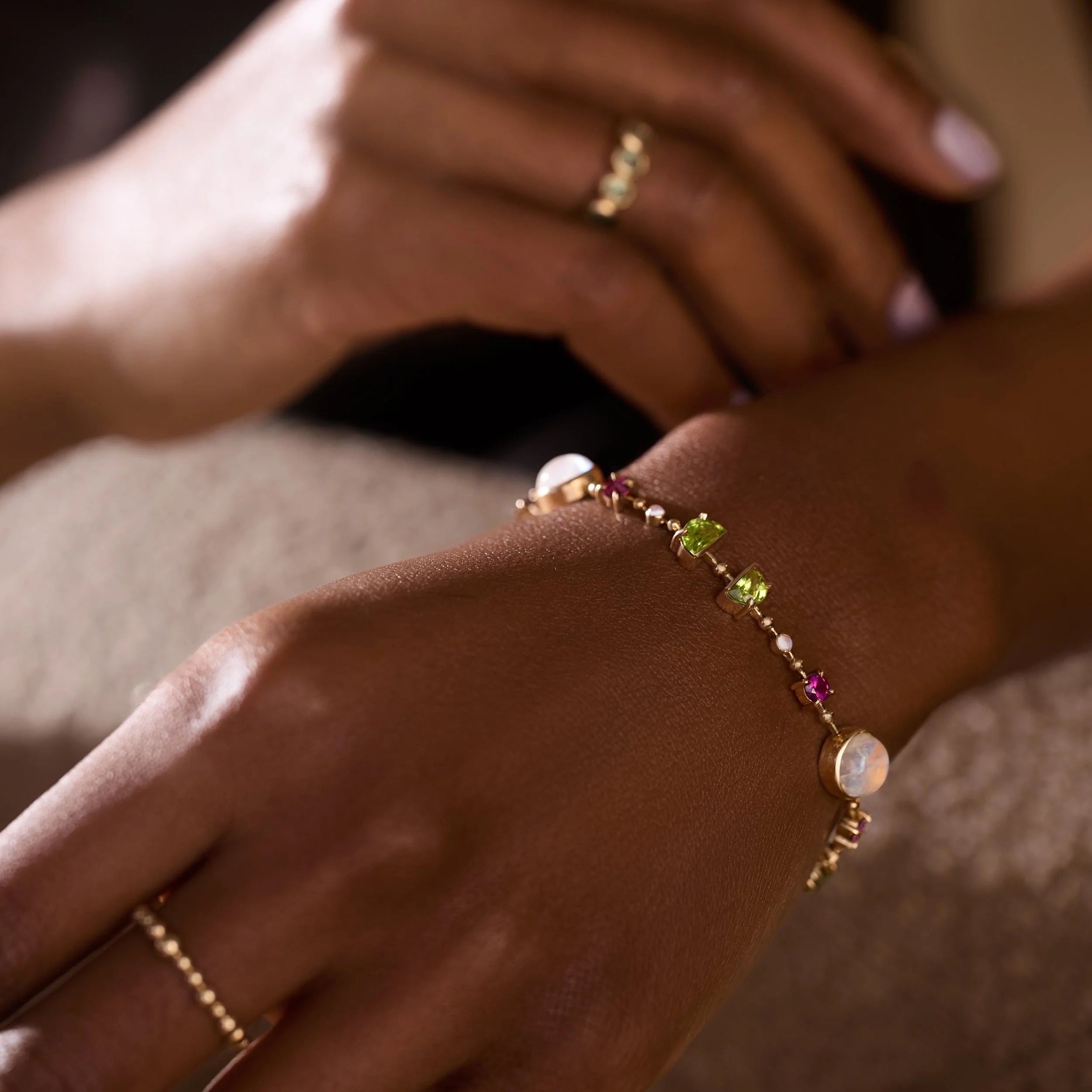 Close-up of a hand wearing a bracelet with colorful gemstones on a neutral background