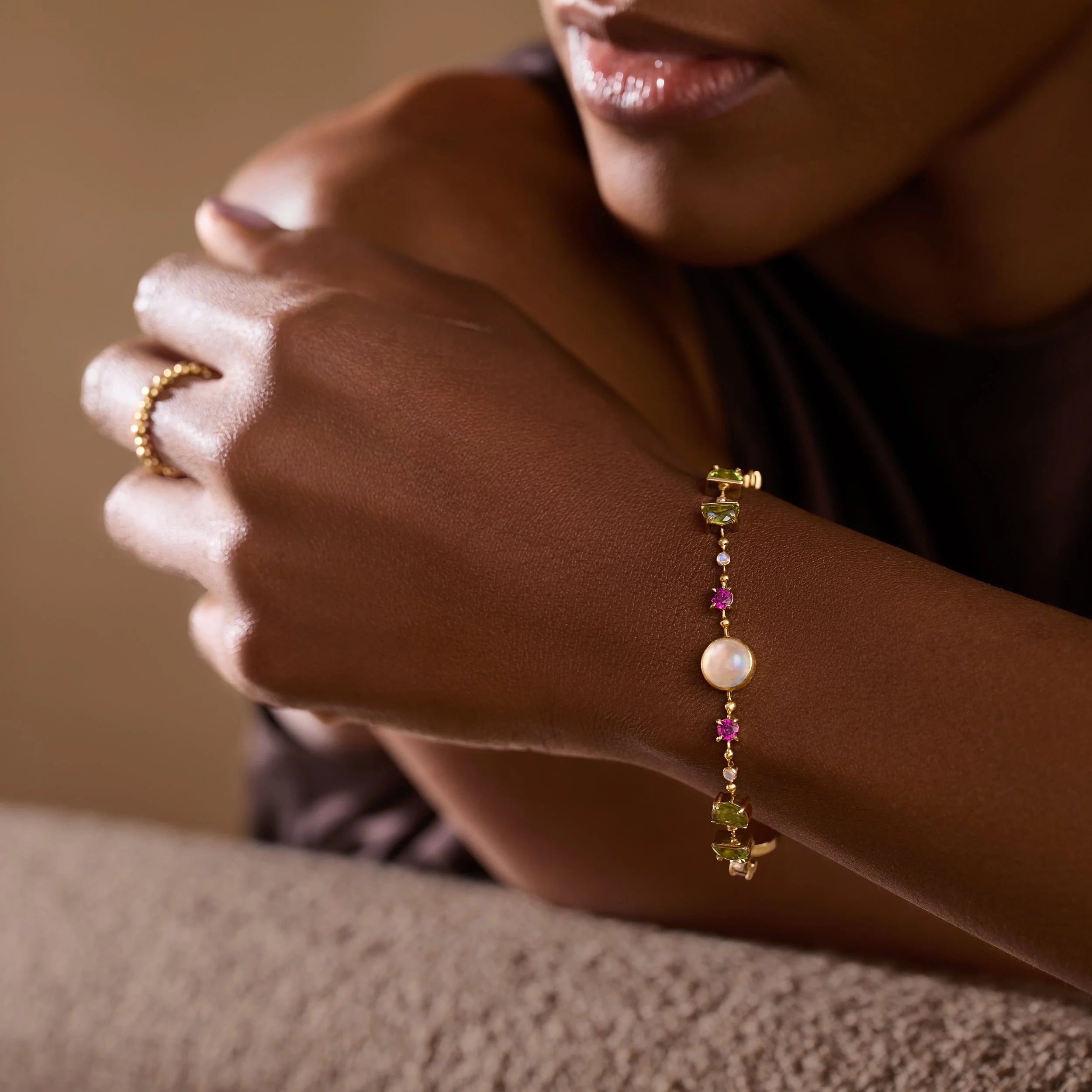 Close-up of a person's hand wearing a bracelet with colorful gemstones on a neutral background