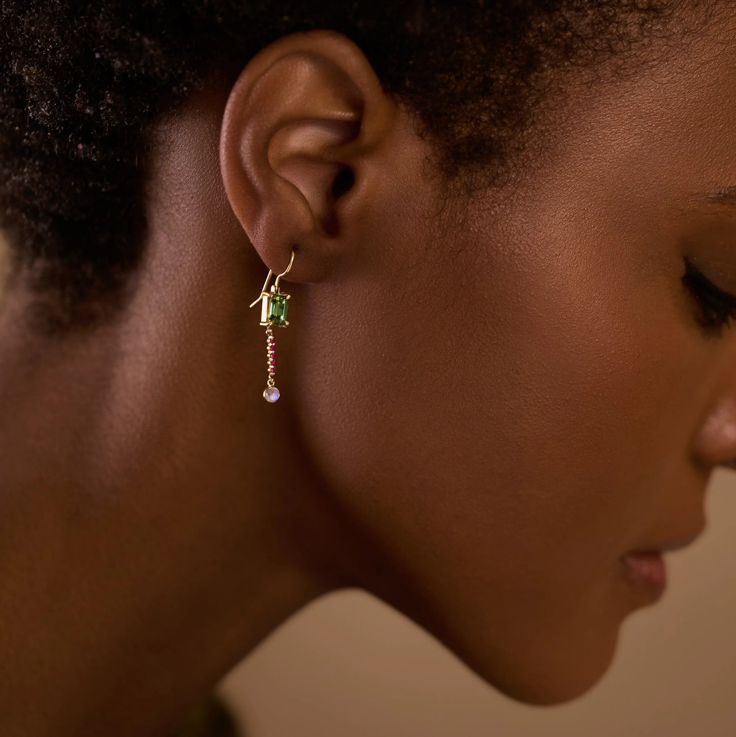 Close-up of a woman wearing a green gemstone earring with a neutral background