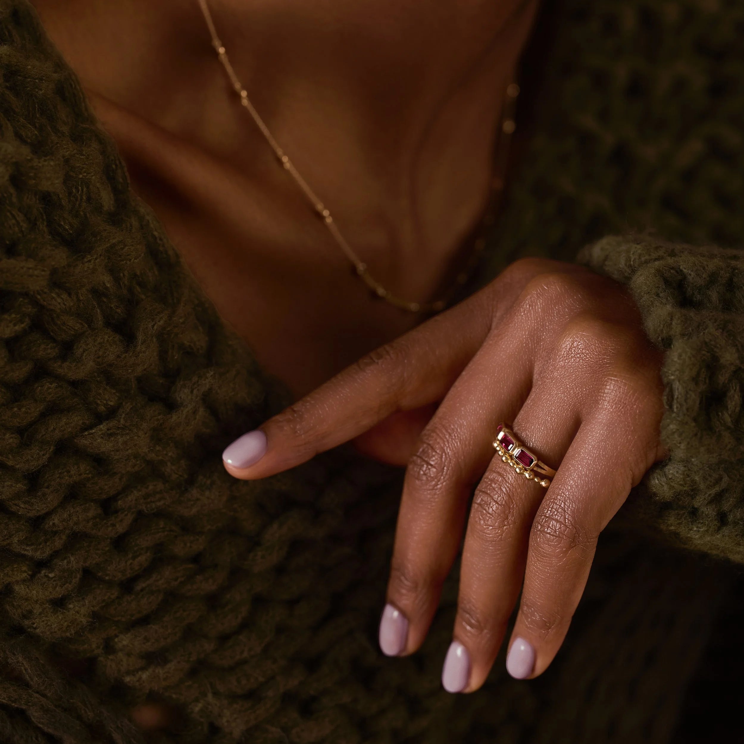 Close-up of a hand wearing a gold ring with purple stones, against a green textured background.