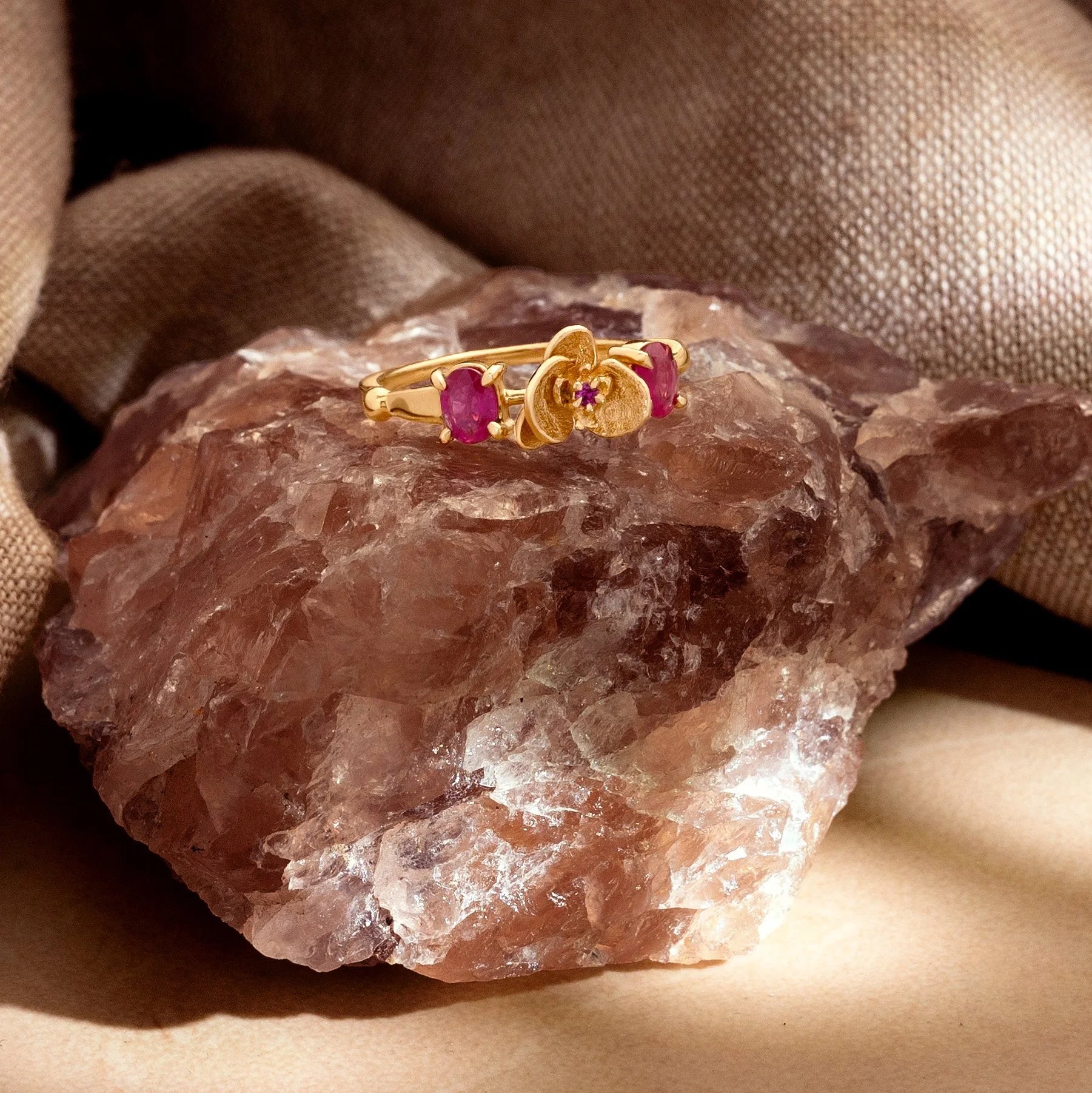 Gold ring with pink gemstones on a large crystal with a beige fabric background
