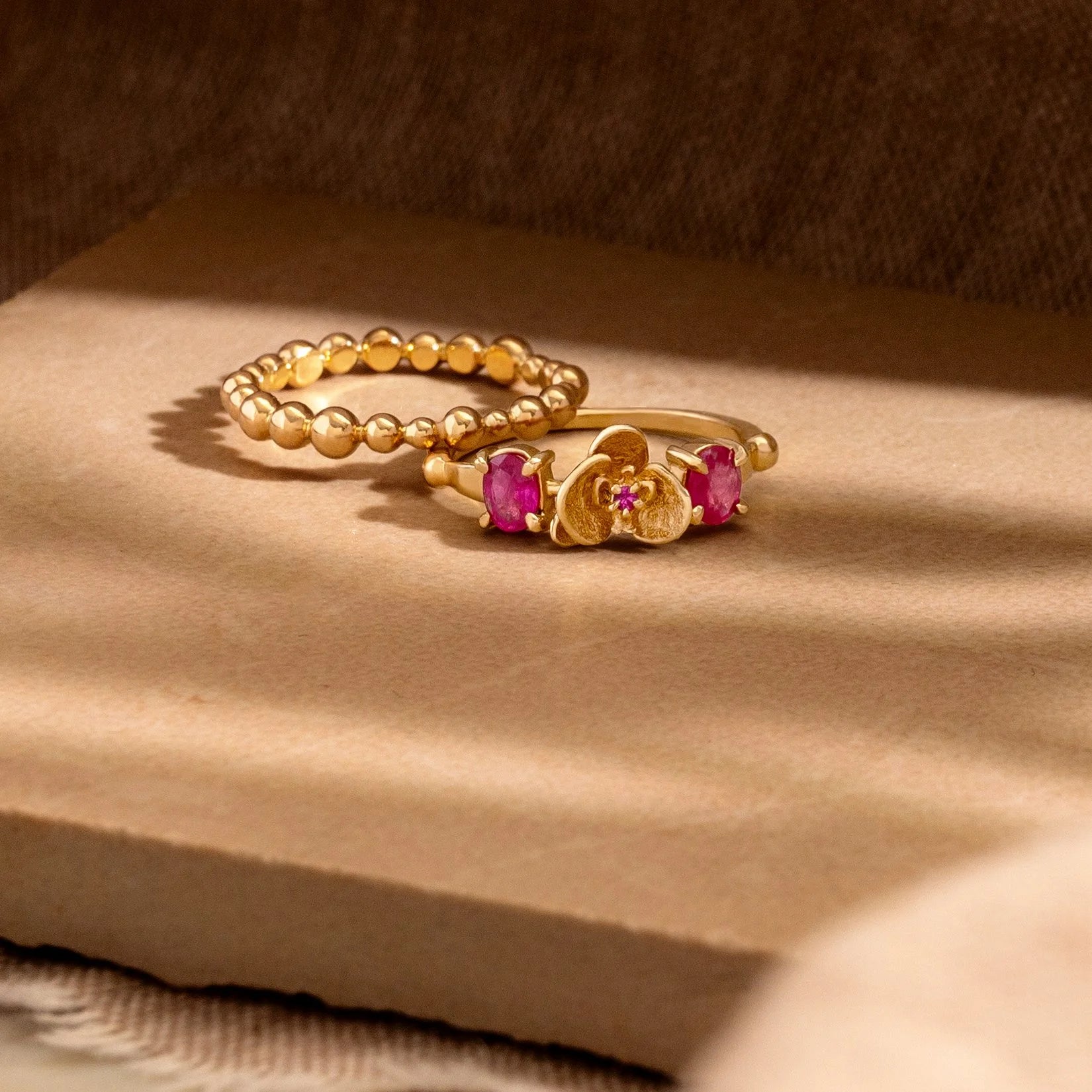 Gold ring with pink gemstones on a beige surface