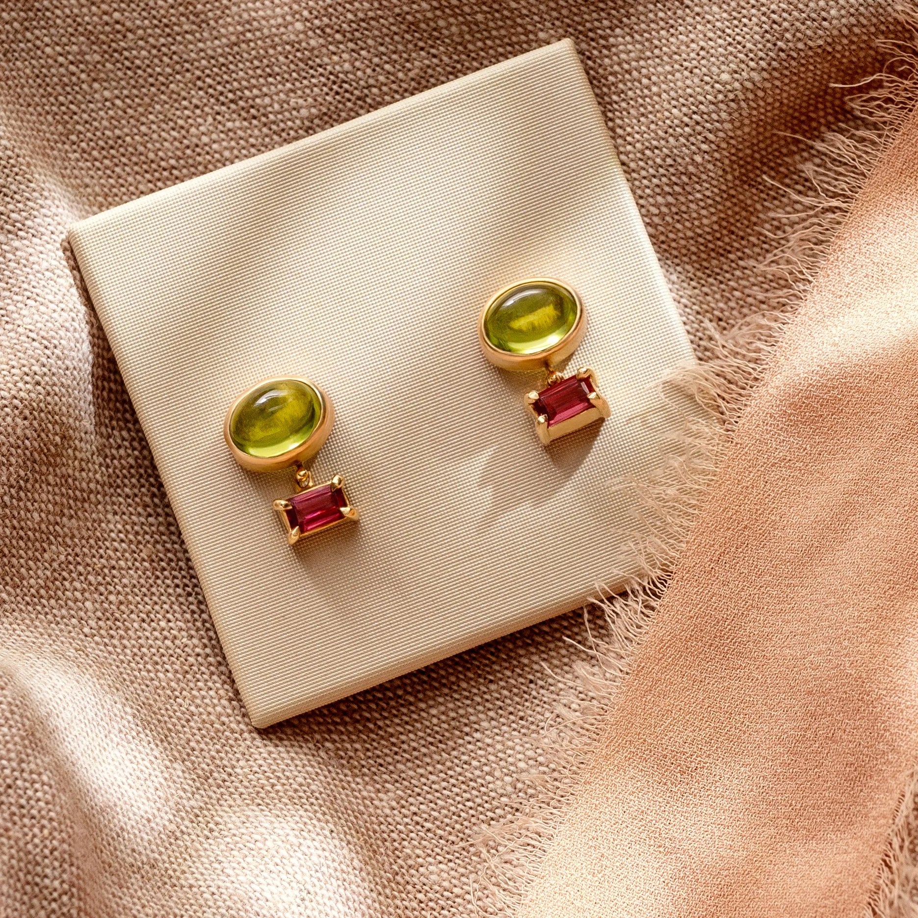Pair of earrings with green and red stones on a beige fabric background