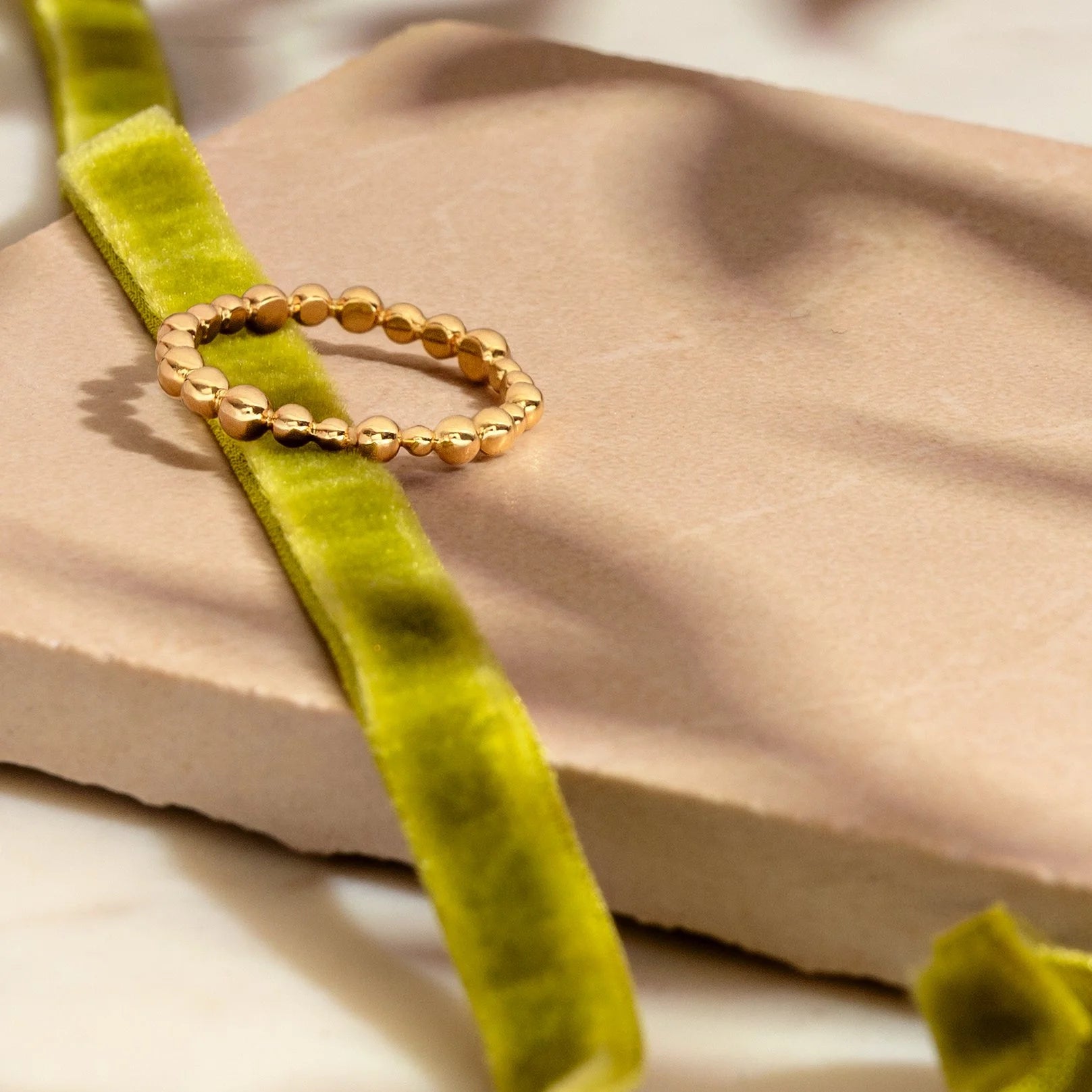 Gold beaded ring on a green velvet ribbon with a beige fabric background