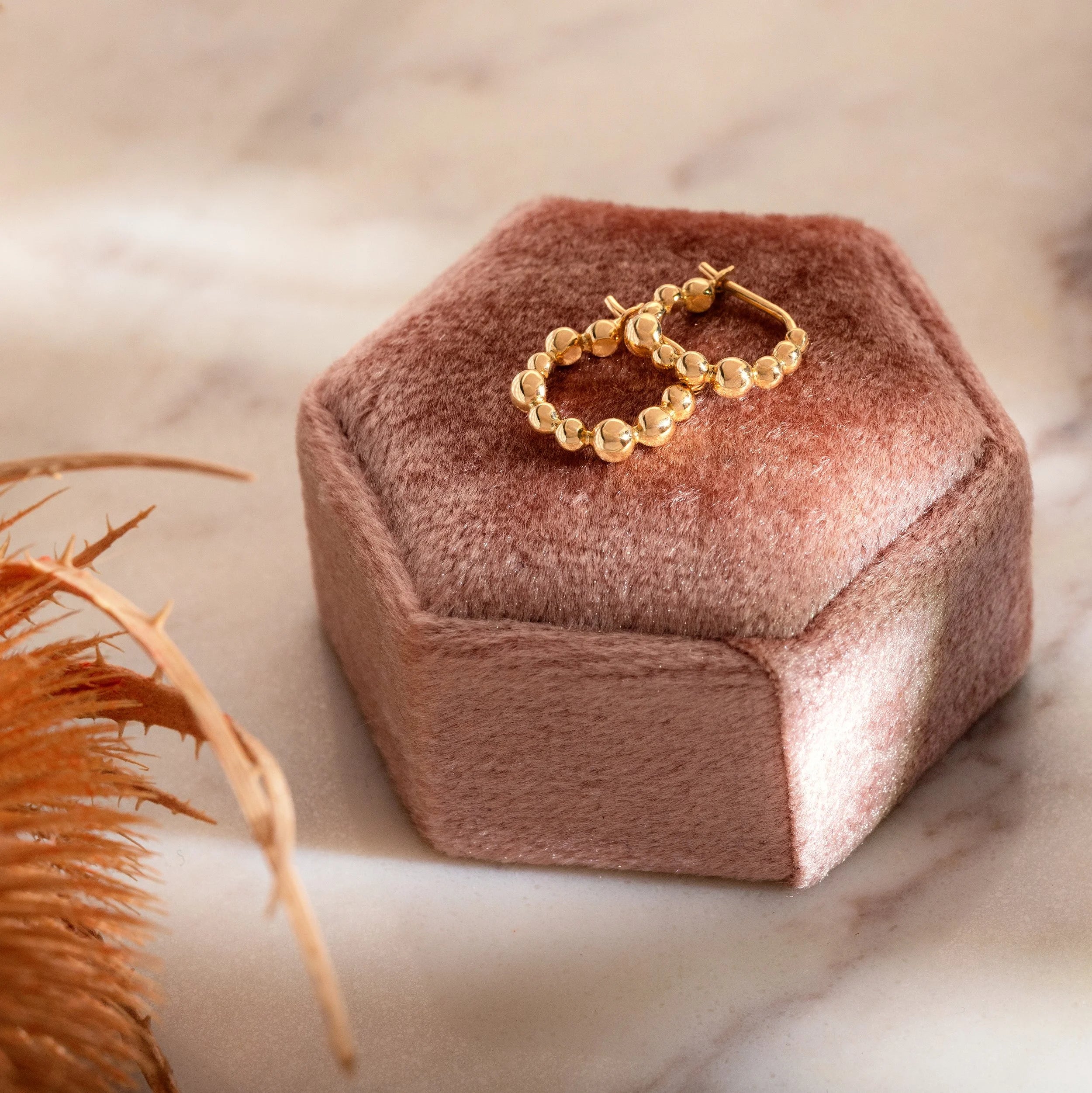 Gold hoop earrings on a hexagonal pink velvet jewelry box with a blurred background