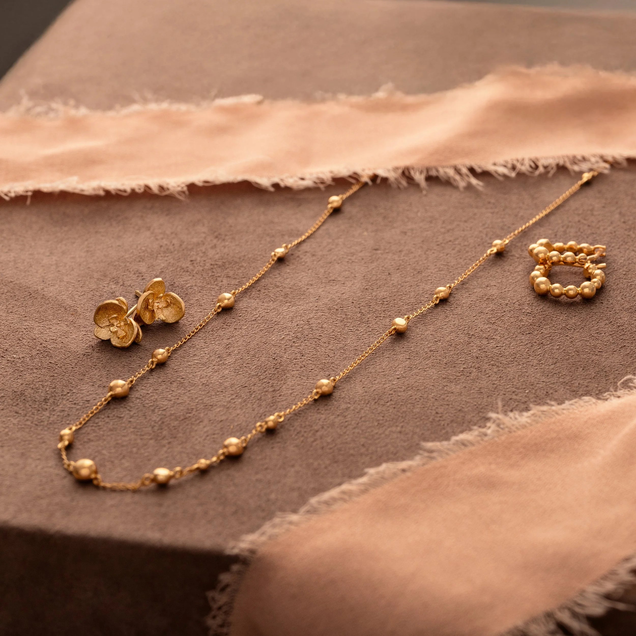 Gold necklace and earrings on a textured brown surface