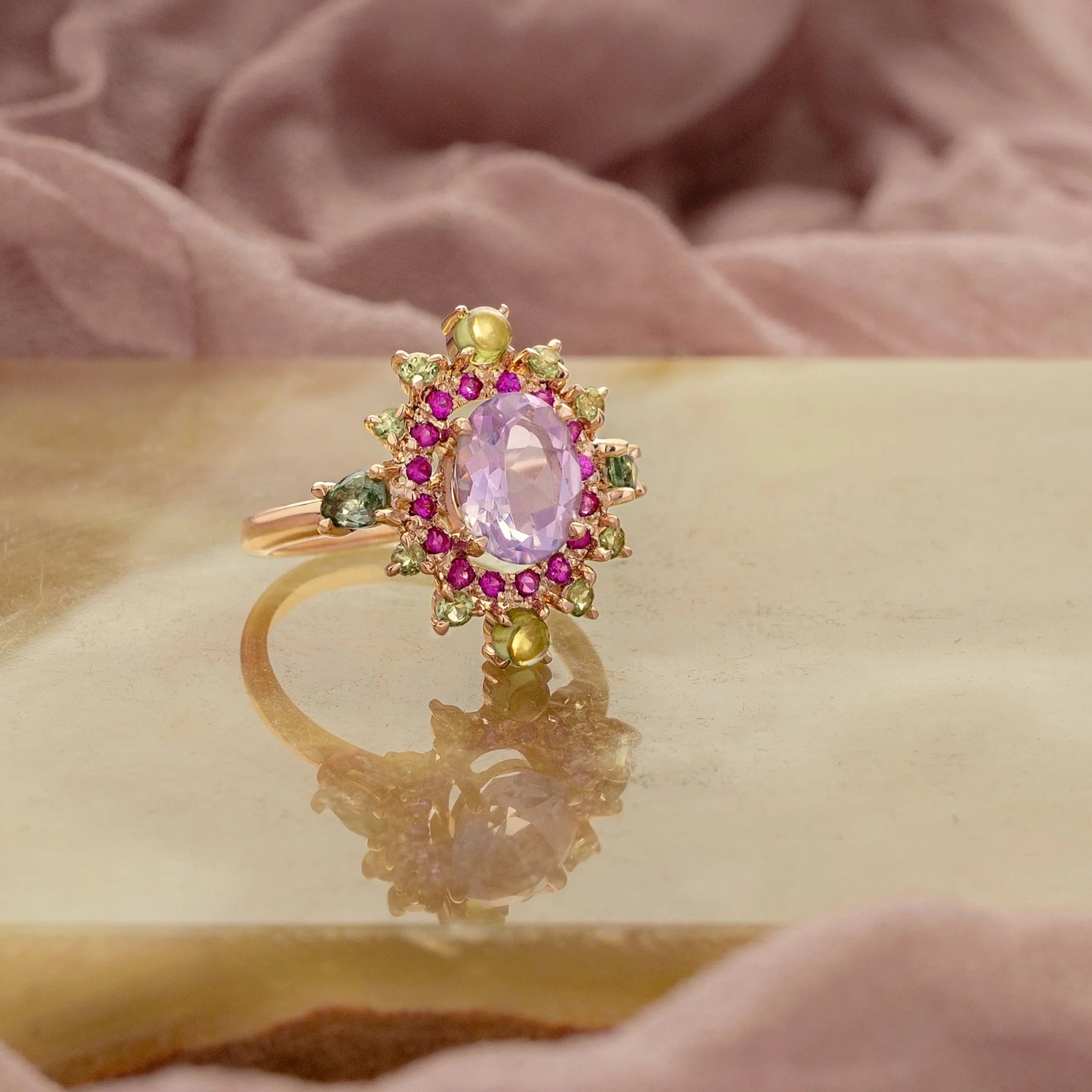 Gold ring with a pink gemstone and colorful accents on a reflective surface.