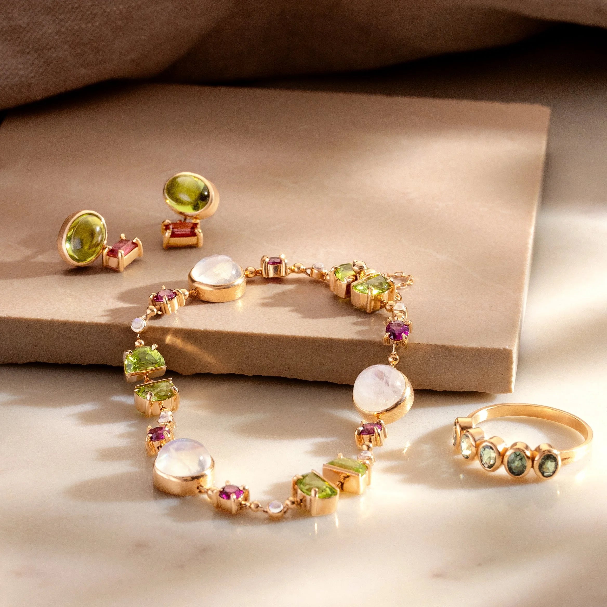 Gold jewelry set with green and purple gemstones on a beige surface