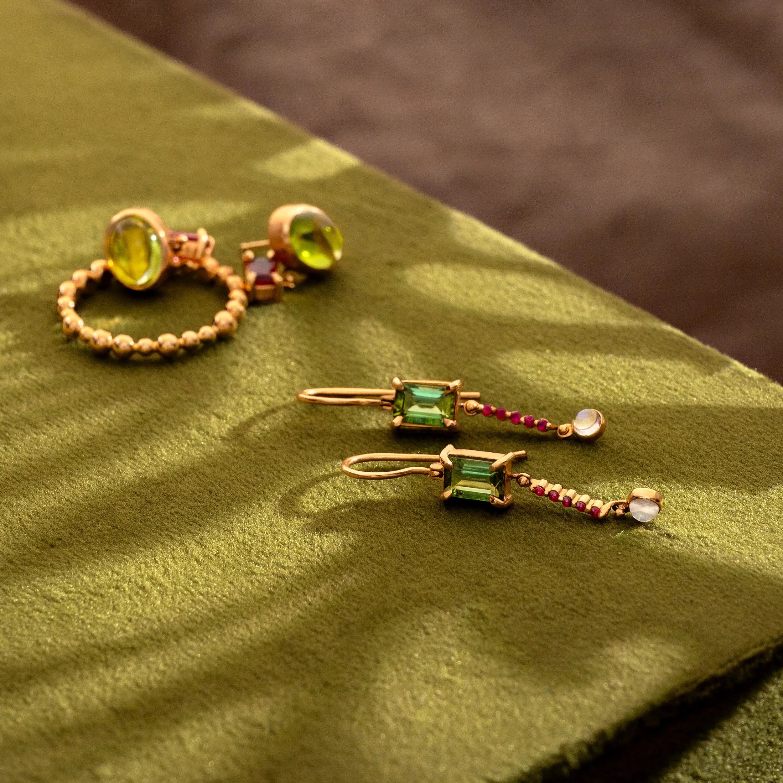 Gold earrings with gemstones on a green fabric background