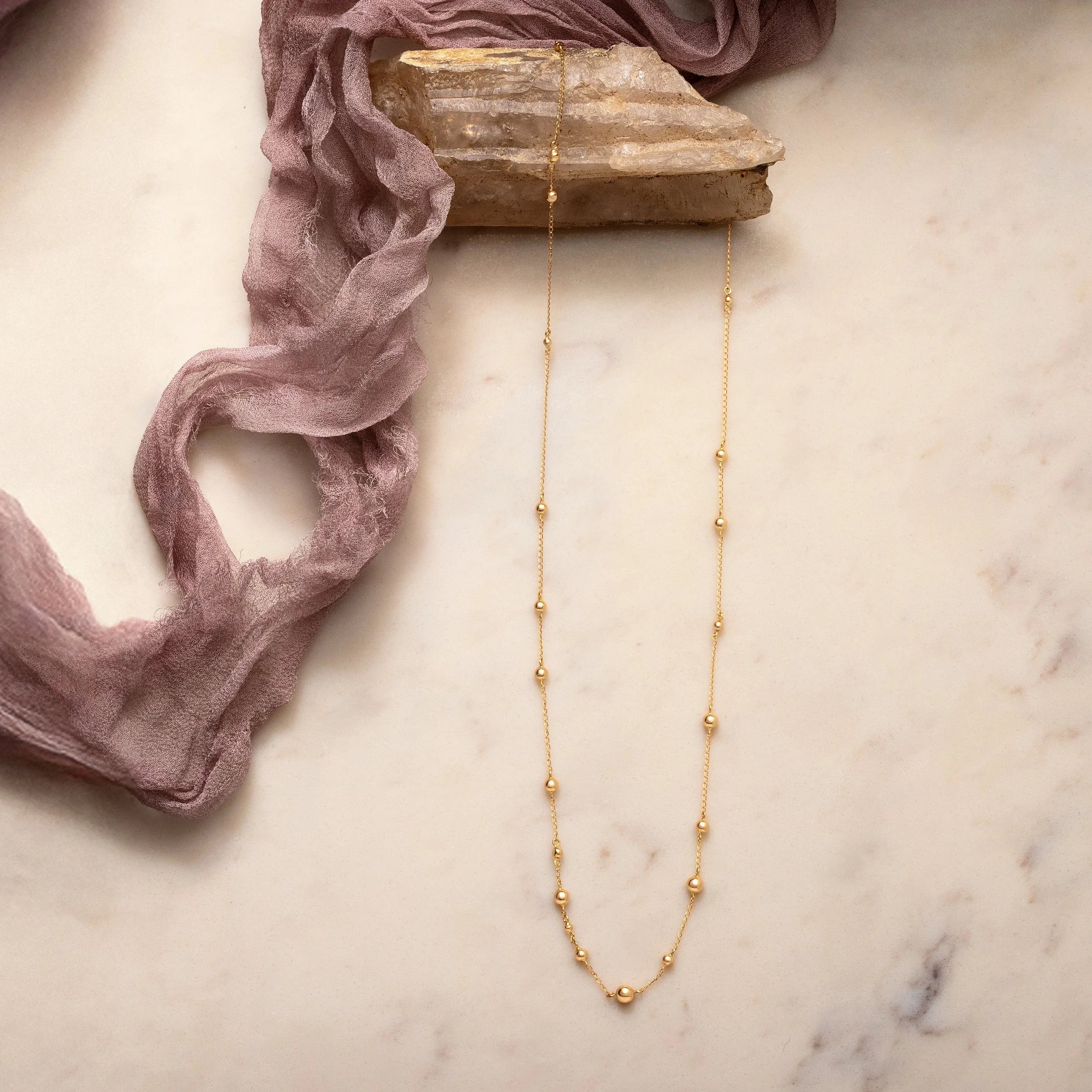 Gold necklace on a marble surface with pink fabric