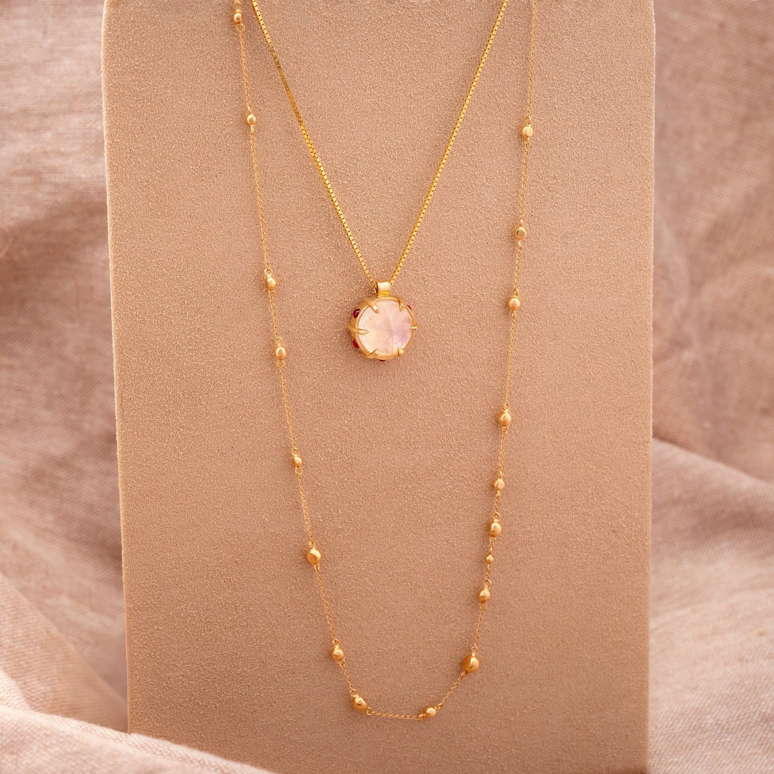 Gold necklace with a pink gemstone pendant on a beige background