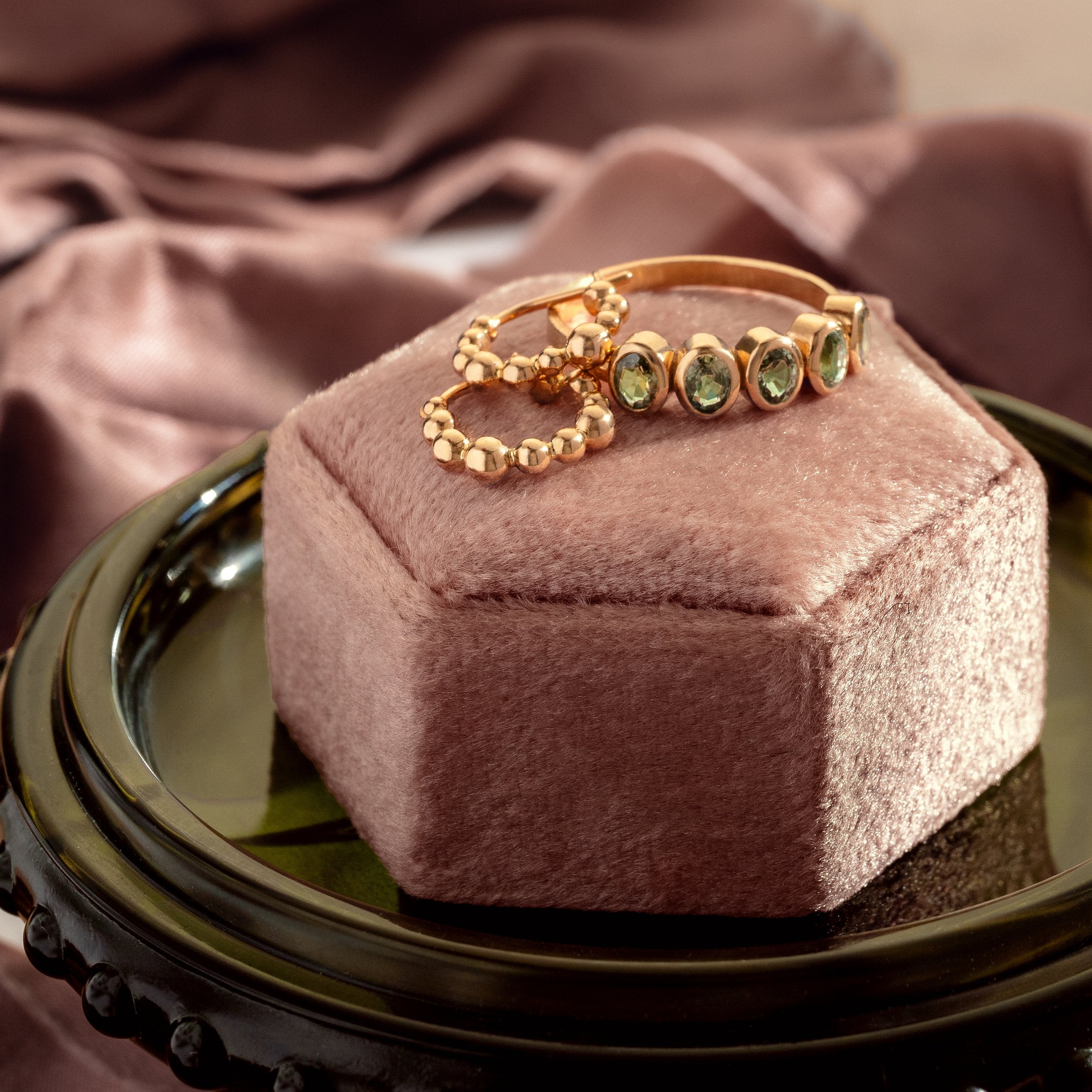 Gold ring with green gemstones on a pink velvet box