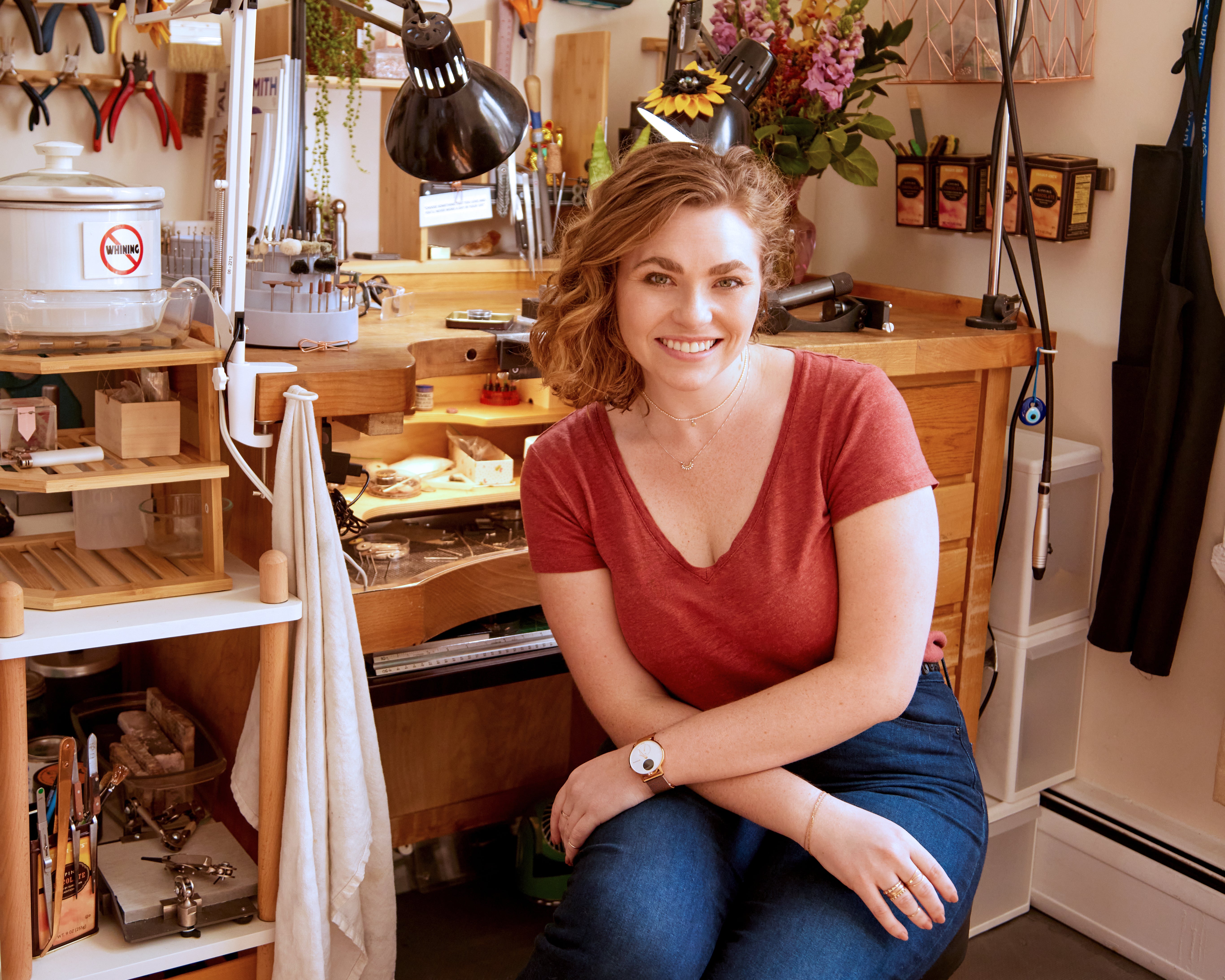 Woman sitting in a jewelry shop with tools and production bench in the background