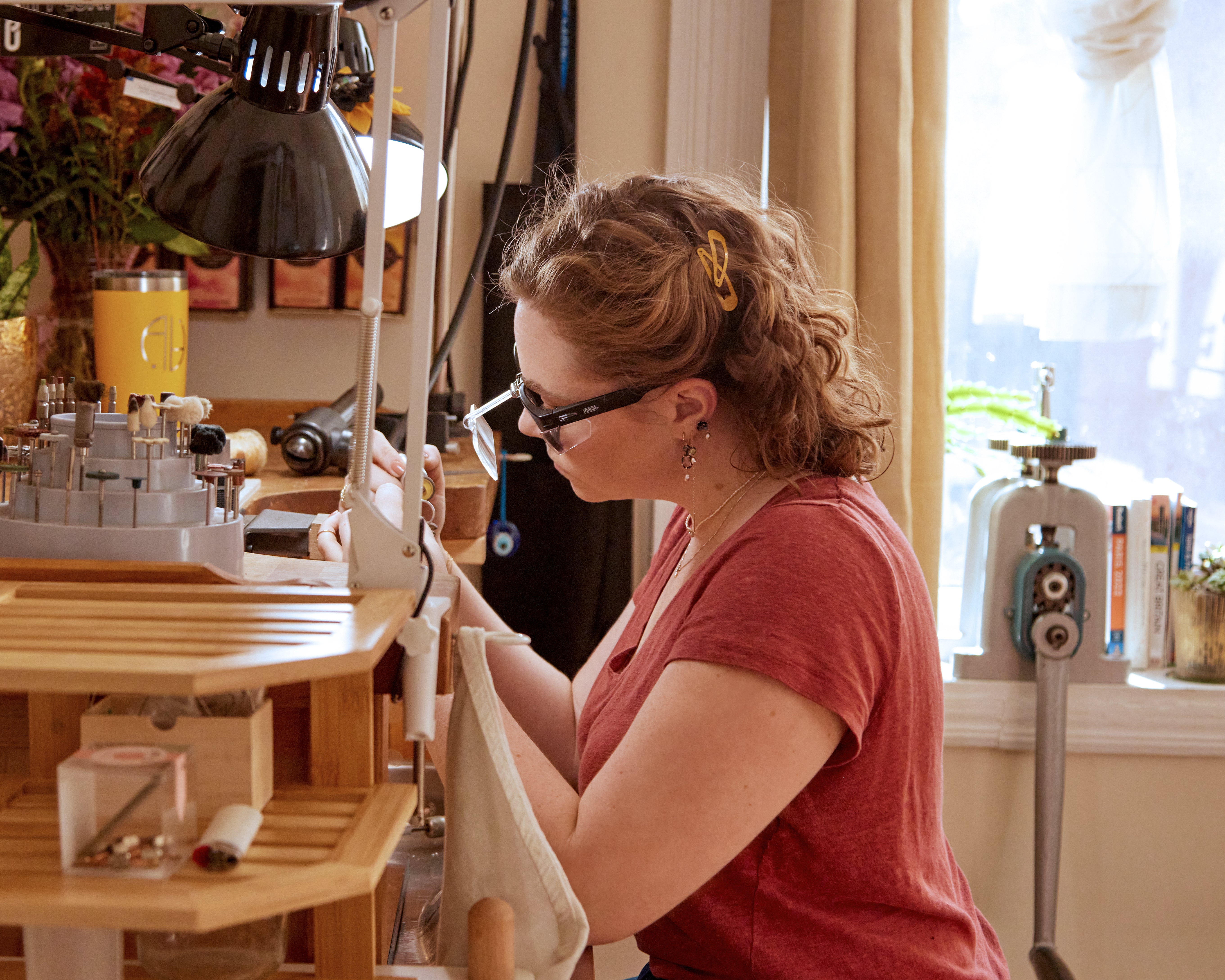 Woman sitting at a jewelry bench in a production studio with various tools around