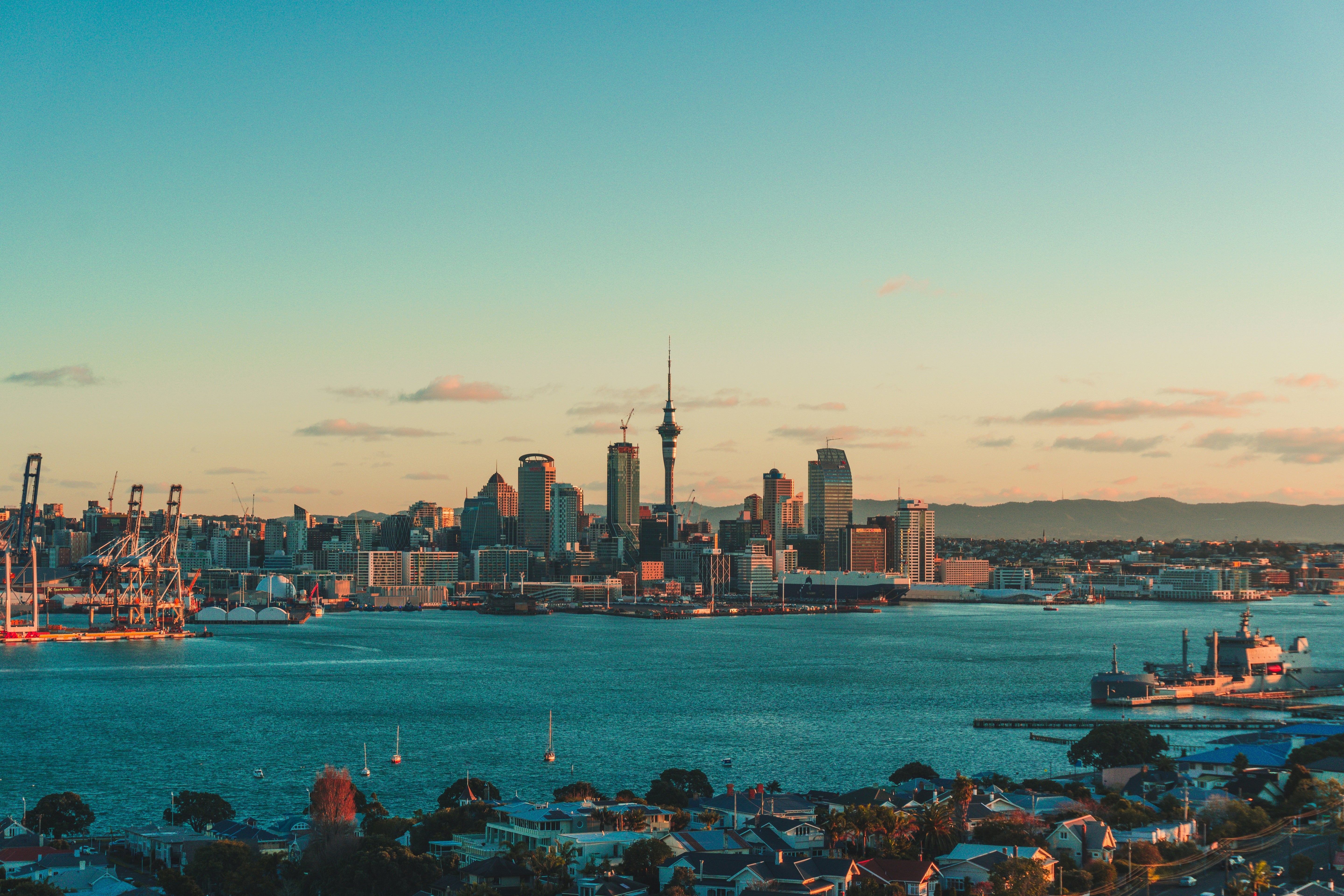 City skyline with a prominent Auckland sky tower over a body of water during sunset.