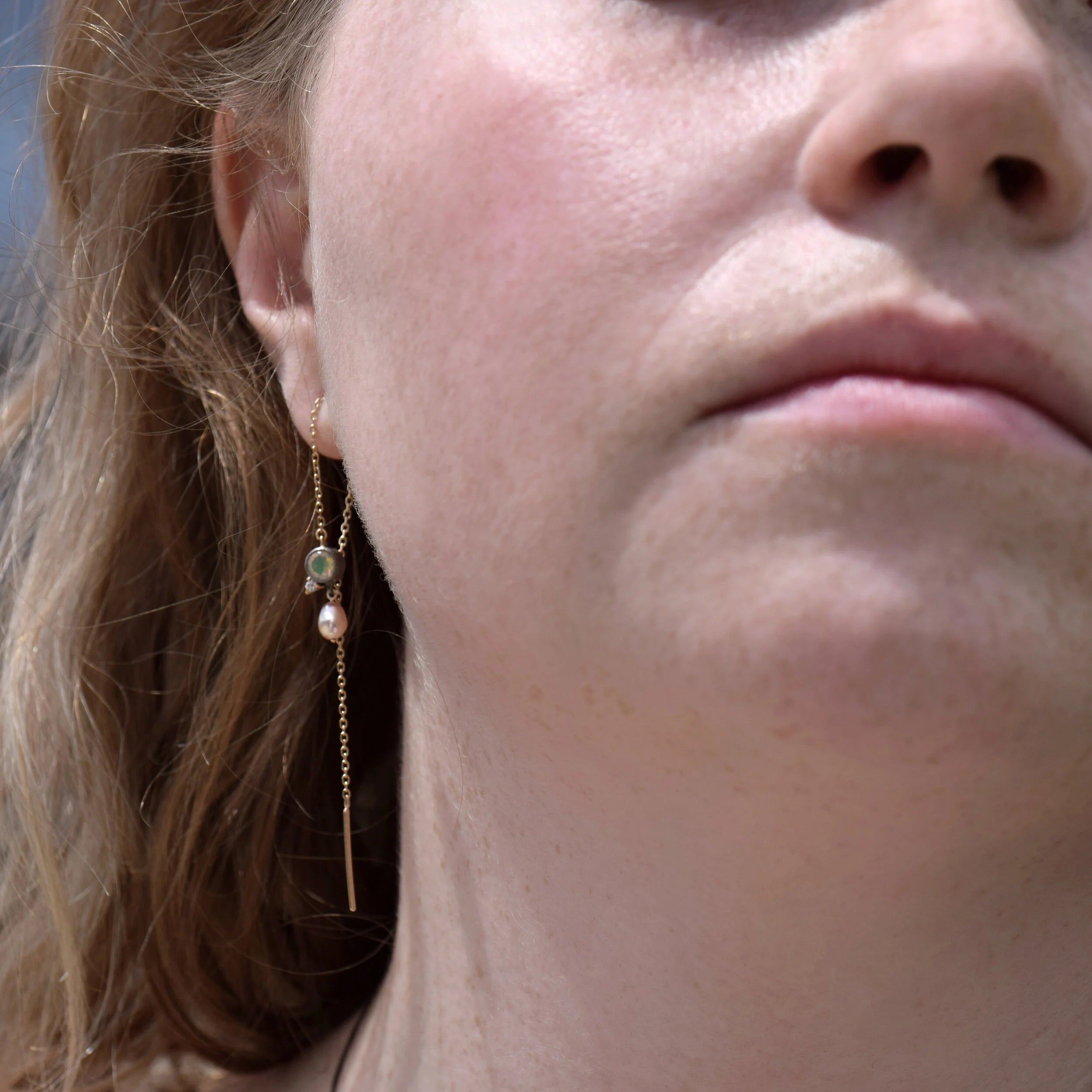 Close-up of a person wearing a delicate gold earring with a small pearl and green gemstone.