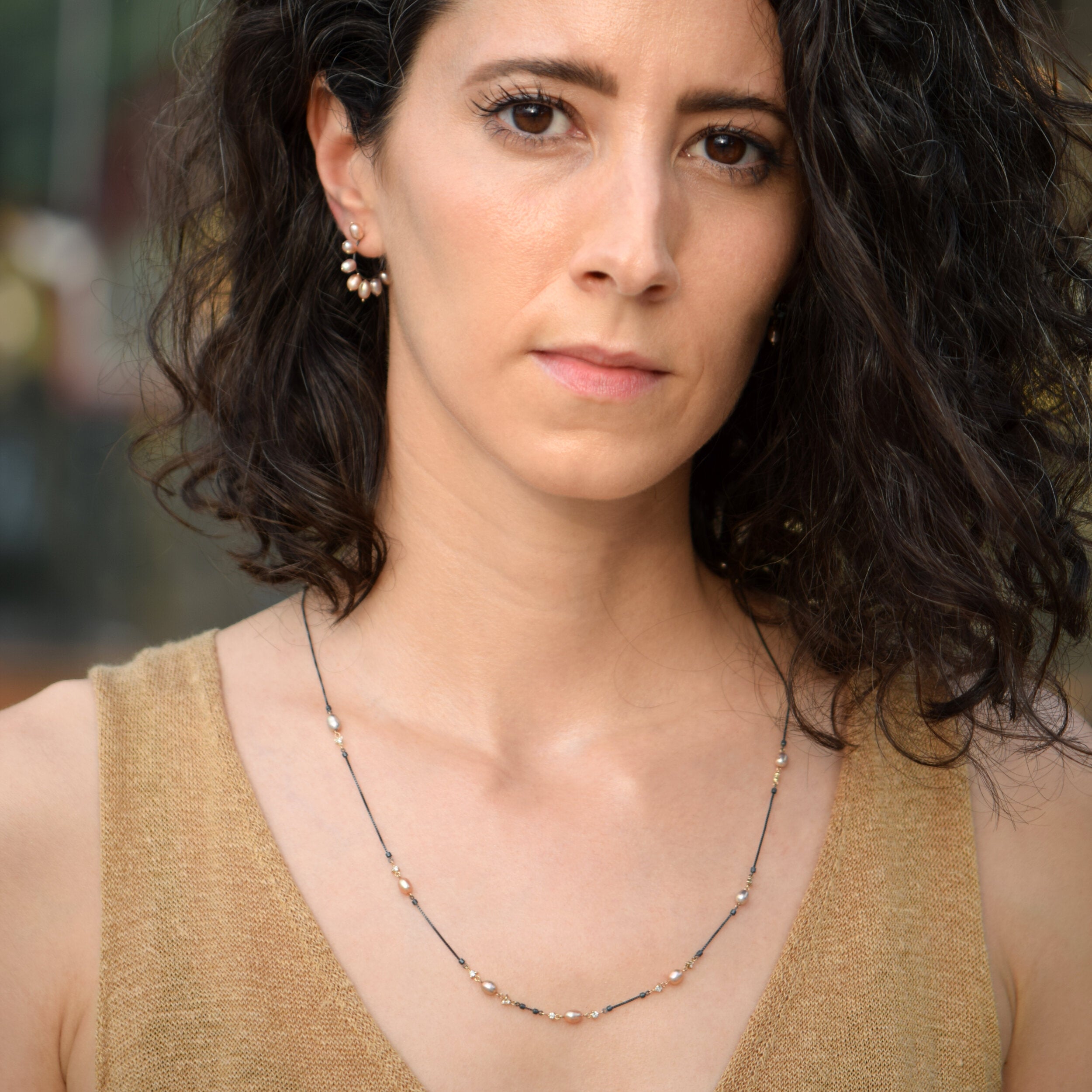 Woman wearing a gold tank top and necklace with a blurred background