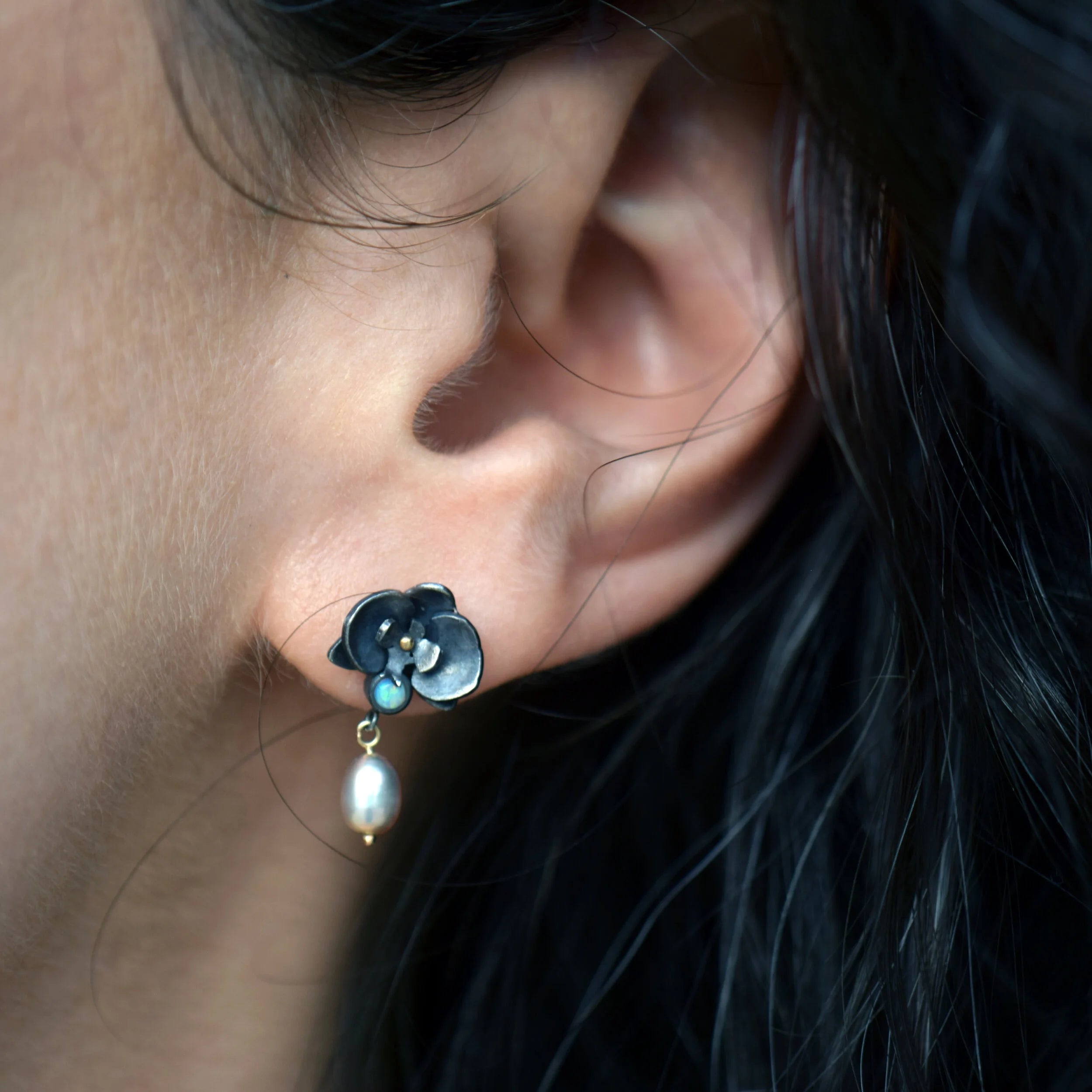 Close-up of an ear wearing a floral earring with a pearl drop.