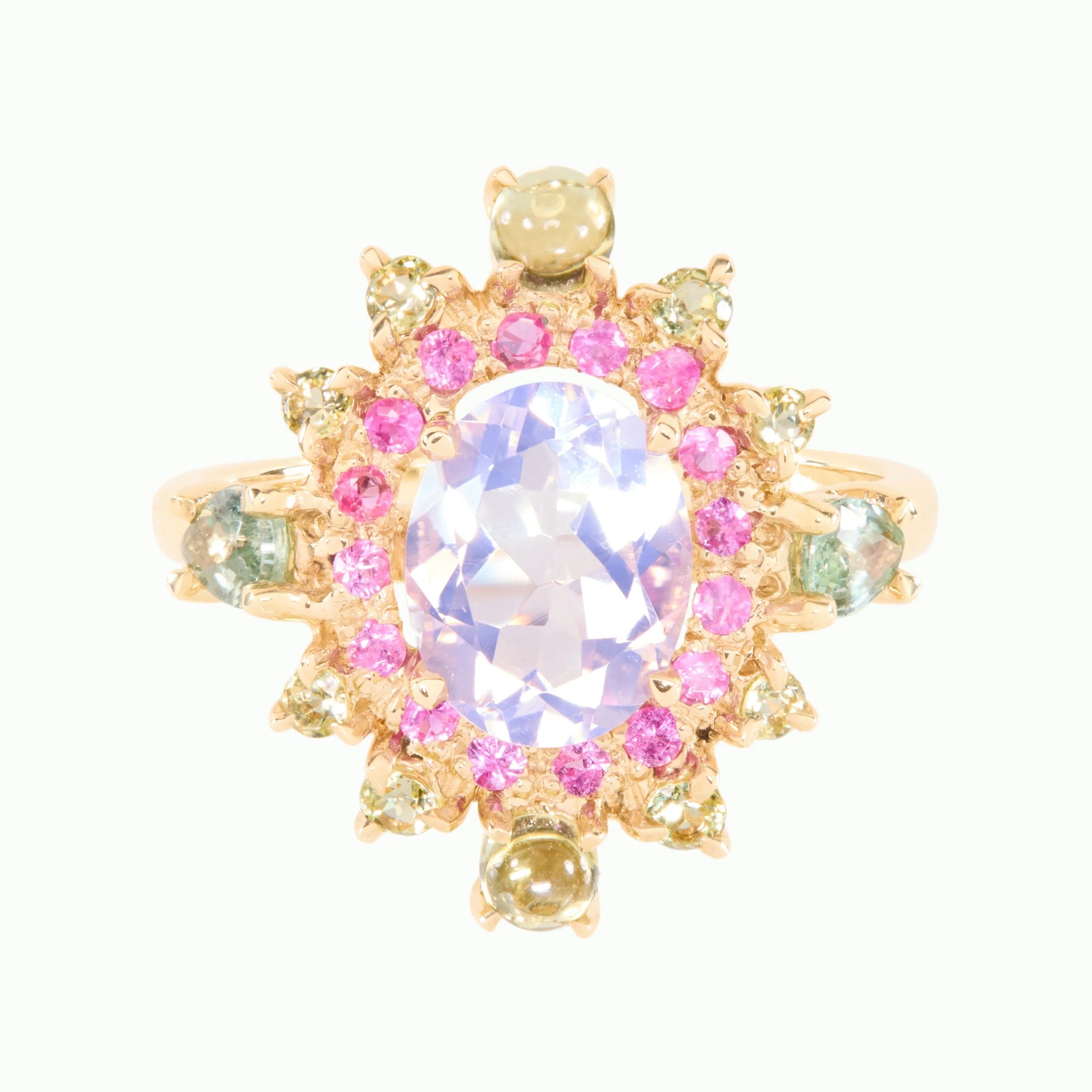 A gold ring featuring a large oval pale lavender center stone surrounded by a halo of pink and light green stones, with smaller gold accents, set against a plain white background.